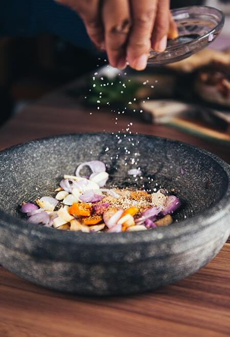 Chopped spices in a stone mortar with salt being sprinkled
